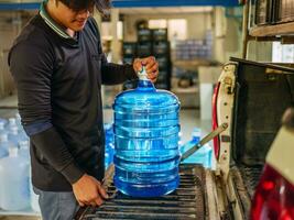 lavoratori sollevamento potabile acqua chiaro e pulito nel blu plastica gallone in il indietro di un' trasporto camion purificato potabile acqua dentro il produzione linea piccolo attività commerciale foto
