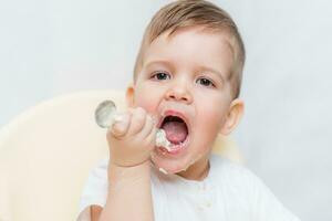 adorabile bambino ragazzo mangia porridge con un' piccolo cucchiaio lui stesso foto