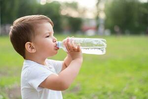 bambino bevande acqua a partire dal un' bottiglia su un' caldo estate giorno foto