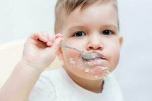 adorabile bambino ragazzo mangia porridge con un' piccolo cucchiaio lui stesso foto