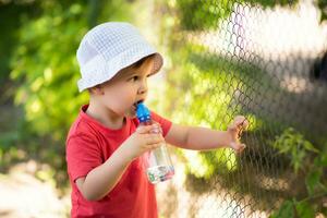 bello ragazzo bevande chiaro acqua a partire dal un' bottiglia su un' soleggiato giorno al di fuori foto