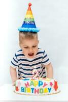 poco ragazzo colpi un' candela su il torta su il suo compleanno foto