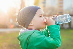 bellissimo bambino bevande acqua a partire dal un' bottiglia su un' caldo estate giorno foto