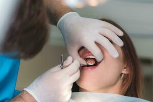 medico ortodontista esamina il orale cavità di un' bellissimo paziente foto