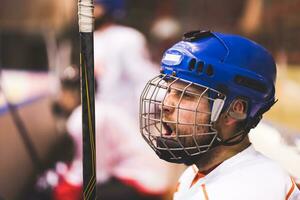 hockey giocatore mantiene urlando il suo squadra seduta su il panchina foto