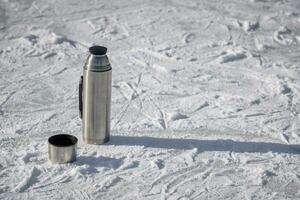 il thermos sta su ghiaccio con un' tazza di caldo tè foto