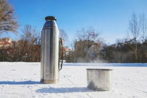 il thermos sta su ghiaccio con un' tazza di caldo tè foto