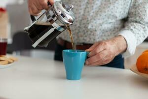 vicino su di anziano uomo godendo un' caldo bevanda dopo scrosciante caffè nel tazza durante prima colazione seduta nel moderno cucina. anziano persona nel il mattina potabile fresco Marrone caffè espresso a partire dal Vintage ▾ boccale foto