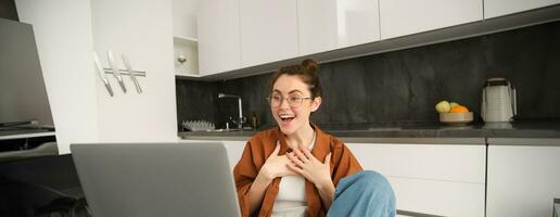 ritratto di giovane donna Lavorando a partire dal casa, seduta a casa con computer portatile, parlando con amico su computer, in linea chattare, si connette per video conversazione foto