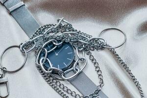 elegante argento catena decorazioni per il collo e orologio su un' seta brillante sfondo. foto
