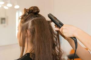 vicino su di dello stilista mano utilizzando arricciatura ferro per capelli riccioli. foto