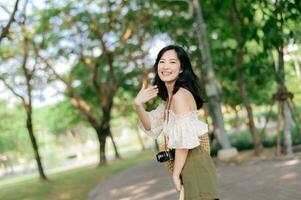 ritratto di asiatico giovane donna viaggiatore con tessitura cappello e cestino e un' telecamera su verde pubblico parco natura sfondo. viaggio viaggio stile di vita, mondo viaggio esploratore o Asia estate turismo concetto. foto