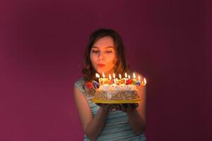 giovane donna soffiaggio su candele su un' compleanno torta al di sopra di rosso sfondo. foto