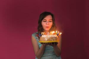 giovane donna soffiaggio su candele su un' compleanno torta al di sopra di rosso sfondo. foto