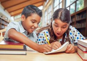 Due ispanico scuola bambini nel un' biblioteca eccitato di loro compiti a casa foto