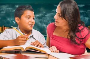 femmina scuola insegnante fare compiti a casa con un' giovane ispanico ragazzo nel il aula. foto