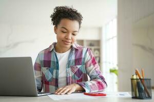 focalizzata nero ragazza studi con il computer portatile e Appunti nel un' luminosa casa ambientazione foto