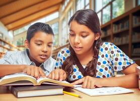 Due ispanico scuola bambini studiando con loro libri nel un' biblioteca foto