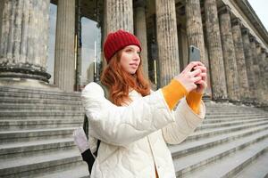 ritratto di giovane blogger, testa Rossa ragazza turista prende immagini di giro turistico, fa fotografie su smartphone telecamera, record video e sorrisi