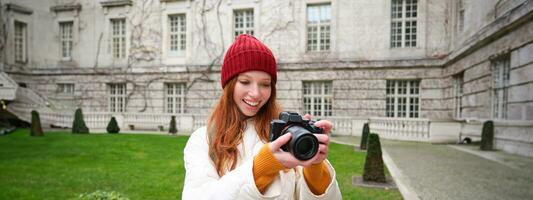 contento testa Rossa ragazza turista, prende fotografie, fotografo con professionale telecamera passeggiate in giro città e cattura bellissimo immagini foto