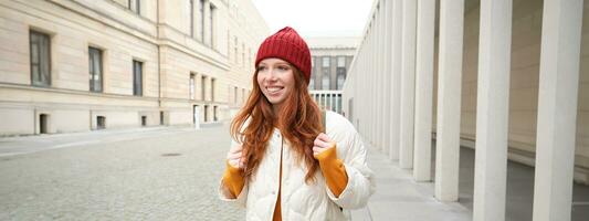 femmina turista nel rosso cappello con zaino, giro turistico, esplora storico punti di riferimento su sua viaggio in giro Europa, sorridente e in posa su strada foto