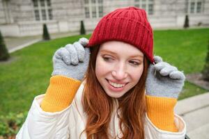 carino ragazza alunno nel rosso cappello, caldo guanti, si siede nel parco, sorrisi e sembra contento. foto