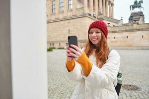 sorridente ragazza turista prende foto di storico punto di riferimento, fa un' foto su smartphone