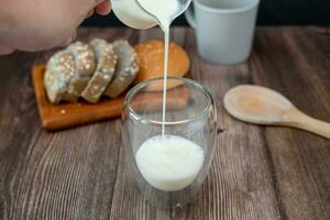 prima colazione impostato maschio mani scrosciante latte su bicchieri e fette di pane. foto