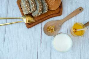 prima colazione impostato miele latte e pane su il legna grano sfondo foto