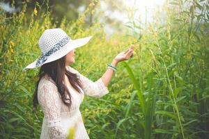 donna asiatica di bellezza in abito bianco e cappello ala camminando sullo sfondo del campo di fiori di colza. relax e concetto di viaggio. benessere felice vita della ragazza in vacanza. natura e stile di vita delle persone foto