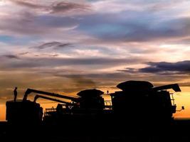 Silhouette di macchine per la raccolta lo scarico di semi di soia in un camion al tramonto, durante il raccolto di una fattoria in Brasile foto