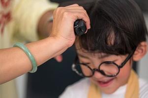 primo piano della mano dello stilista del barbiere che fa un ragazzo asiatico carino per un nuovo stile di capelli con piastra per capelli. stile di vita delle persone e concetto di famiglia. bellezza e moda foto