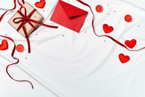 romantico concetto. san valentino giorno sfondo. rosso Busta, regalo scatola e cuori su bianca seta foglio foto