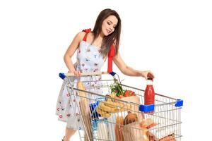 sorridente giovane donna fare drogheria shopping a il supermercato, lei è mettendo un' pomodoro succo bottiglia nel il carrello foto
