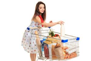 sorridente giovane donna fare drogheria shopping a il supermercato, lei è mettendo un' latte bottiglia nel il carrello foto
