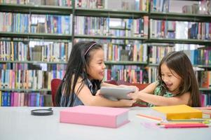 due ragazze che combattono per il tablet in classe mentre leggono libri. stili di vita ed educazione delle persone. giovane amicizia e relazione con i bambini nel concetto di scuola. tema dell'asilo nido e della diversità foto