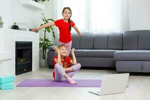 Due poco ragazze praticante yoga, allungamento, fitness di video su taccuino. lontano in linea formazione scolastica addestramento, aerobico a casa. salutare stile di vita, coronavirus, restare casa. bambini sport casa quarantena. foto