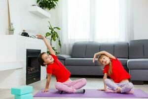 Due poco ragazze praticante yoga, allungamento, fitness di video su taccuino. lontano in linea formazione scolastica addestramento, aerobico a casa. salutare stile di vita, coronavirus, restare casa. bambini sport casa quarantena. foto