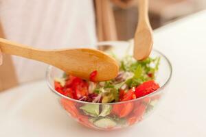 mano miscelazione fresco insalata nel cucina su di legno tavolo. foto
