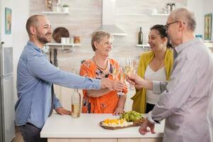 multigenerazione famiglia tintinnante bicchieri con vino nel casa cucina durante riunione. foto