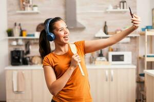 assunzione un' autoscatto e cantando nel il mattina utilizzando di legno cucchiaio. energico, positivo, felice, divertente e carino casalinga danza solo nel il Casa. divertimento e tempo libero solo a casa foto