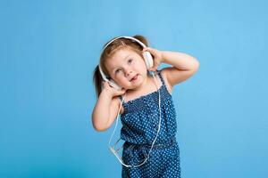 carino poco ragazza nel cuffie ascoltando per musica utilizzando un' tavoletta e sorridente su blu sfondo foto