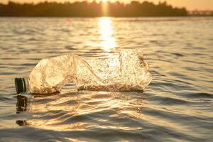 spiegazzato plastica bottiglia galleggia su il superficie di il acqua. tramonto, verde alberi. persone e ecologia. sul fiume inquinamento. avvicinamento sparo. foto