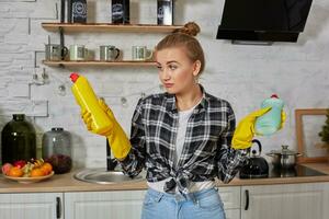 donna confrontando detergente prodotti, lei è Tenere Due bottiglie e controllo loro a casa cucina. foto