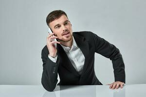 bello giovane uomo parlando su il mobile Telefono mentre seduta a il suo Lavorando posto nel ufficio foto