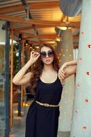 avvicinamento ritratto di giovane elegante brunetta nel nero vestito e occhiali da sole. moda strada tiro foto