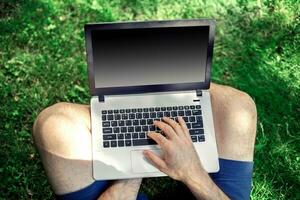 giovane blogger seduta su erba e Lavorando con il computer portatile foto