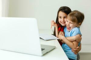 Due ragazze, il il più antico e il minore, siamo impegnato a un' tavolo su un' il computer portatile. foto