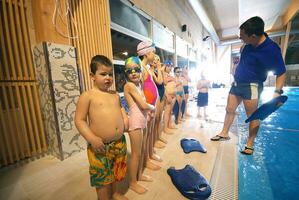 un' gruppo di bambini nel costumi da bagno in piedi nel un' piscina foto