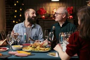 gruppo di persone incontro su Natale per celebrare festivo cena insieme, di stagione dicembre vacanza. giovane e vecchio persone sensazione contento in giro il tavolo con tradizionale cibo e vino. foto